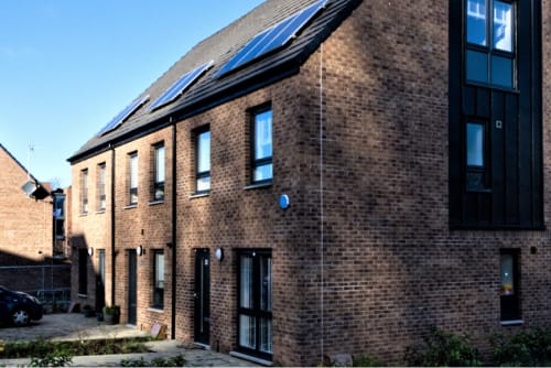 A photo of three terraced homes made of brick. There are solar panels on the roof and they look new and modern.