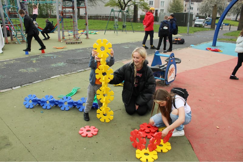 A young woman and two children making sculptures in a playground with hexagonal pieces